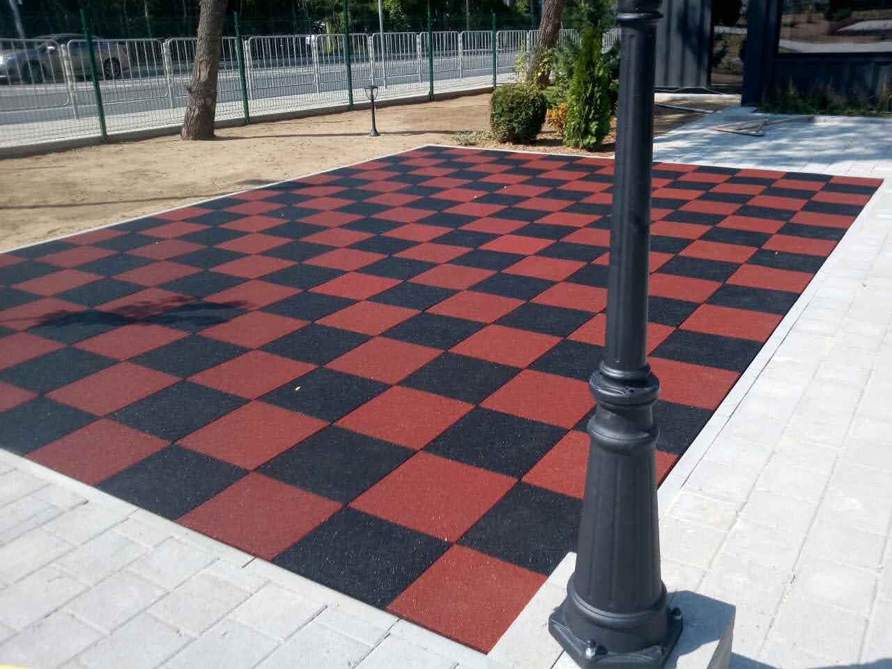 montaj-kauchukova-nastilka-shahmatna-tereno-eko.jpg Installed "Tereno Eco" shock-absorbing rubber flooring in red and black, arranged in a chessboard pattern on a playground.